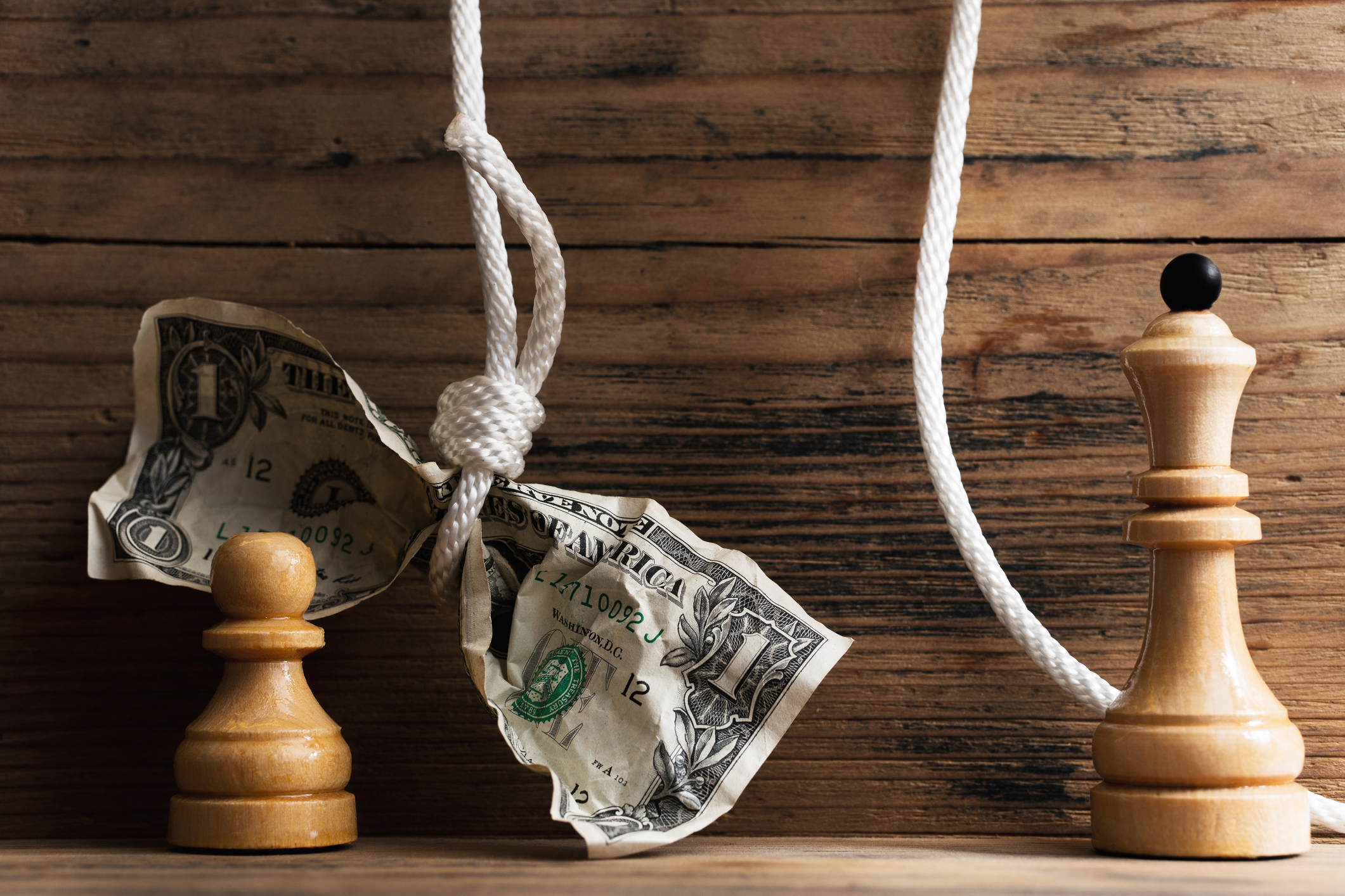 Wooden chessmen and crumpled dollar bill hanging on a tightly knotted white rope