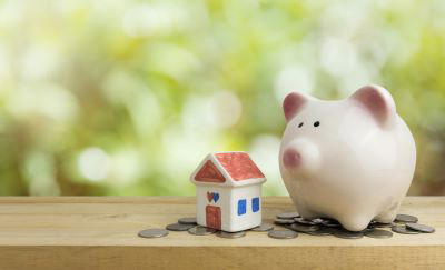 Piggybank on top of coins next to small painted ceramic house