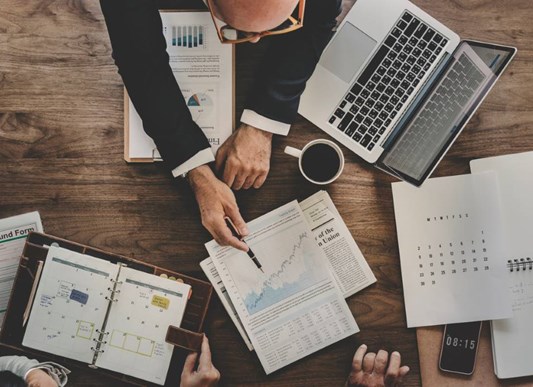 Overhead view of three people looking through graphs and planners on table