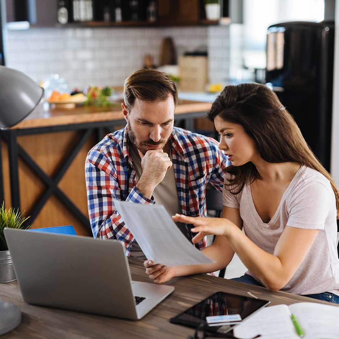 Man and woman looking over a financial sheet sitting at a kitchen table