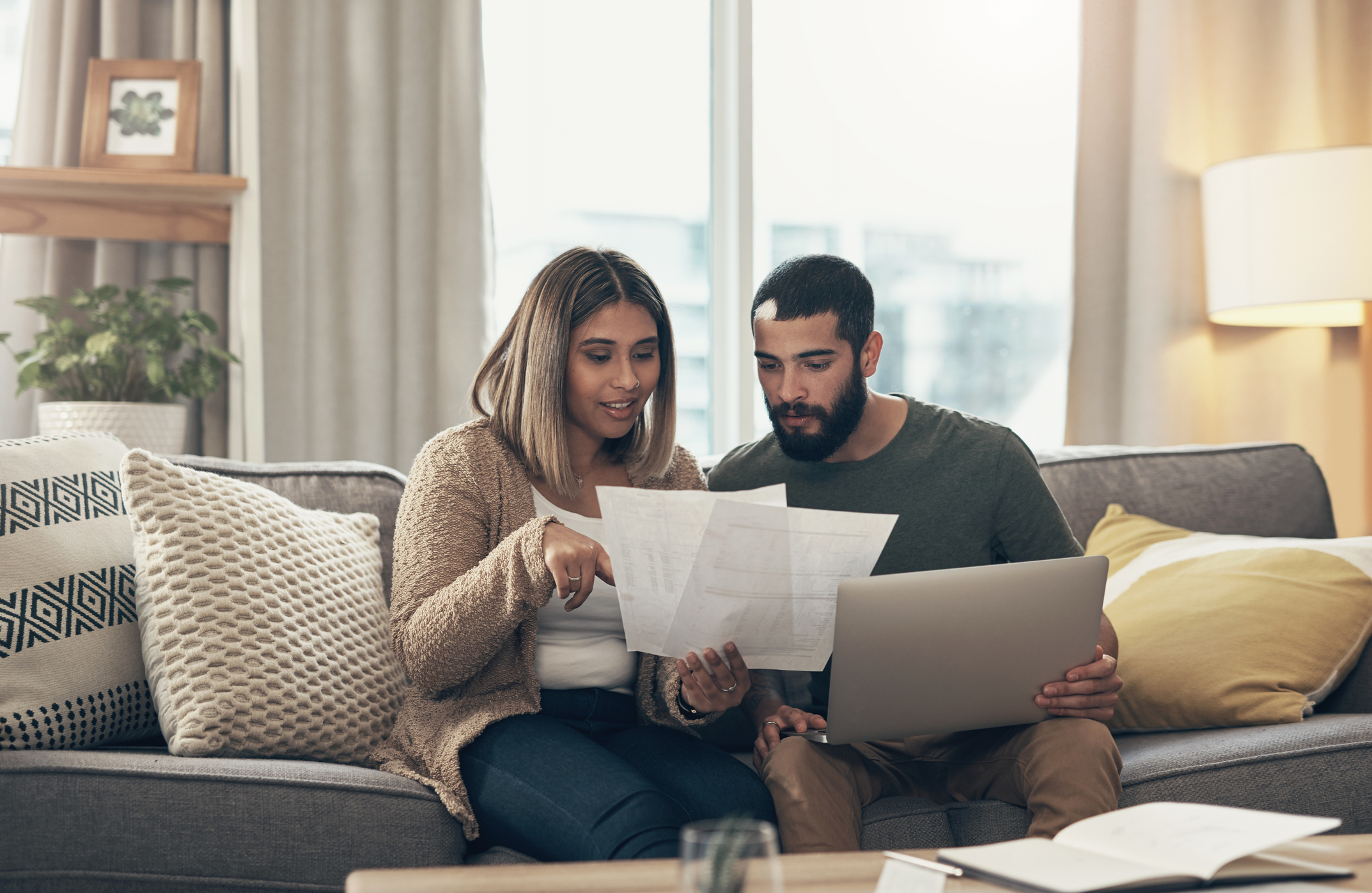 Shot of a young couple using a laptop while going through paperwork at home